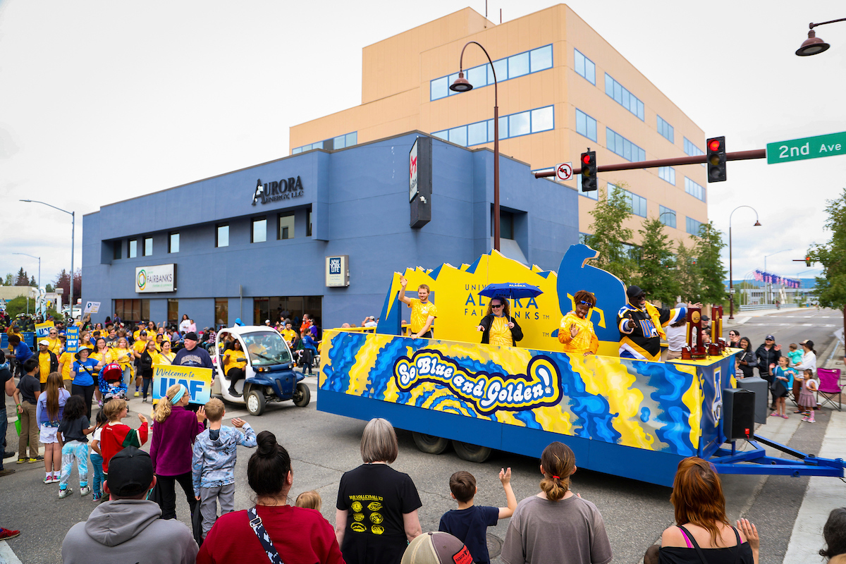 The UAF Golden Days Parade float makes its way through downtown Fairbanks with alumni, staff, and students following close behind.