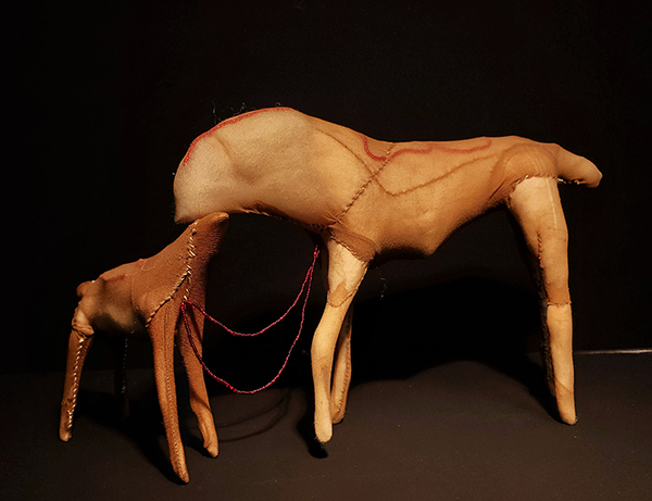 An abstract textile sculpture featuring stitching and beadwork of a moose mother and its baby