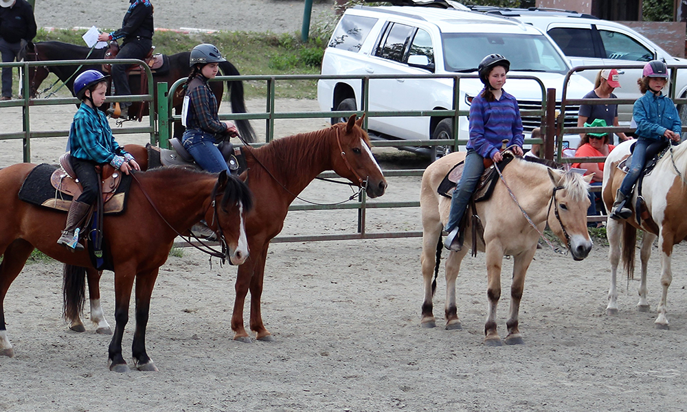 Kids riding horses within a fenced area