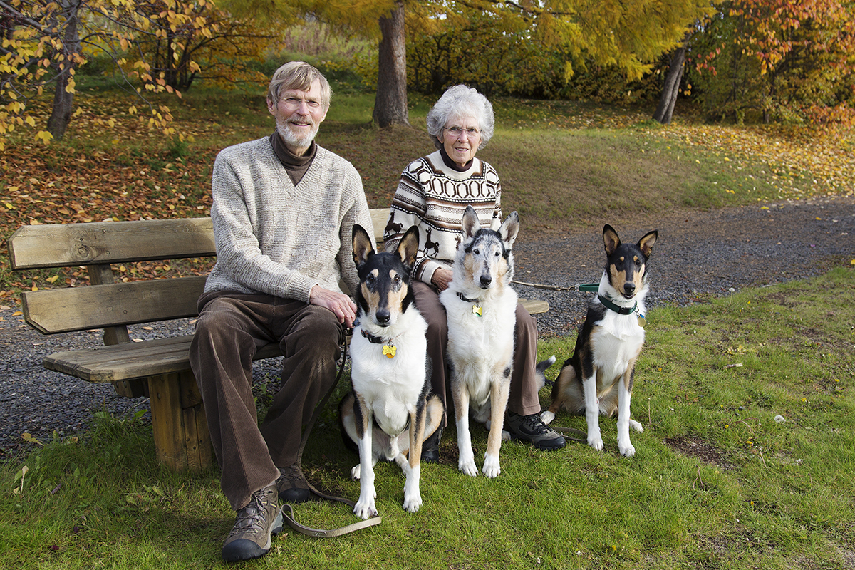 Jon and Jane Aspnes pose on a bench in the park with their three dogs