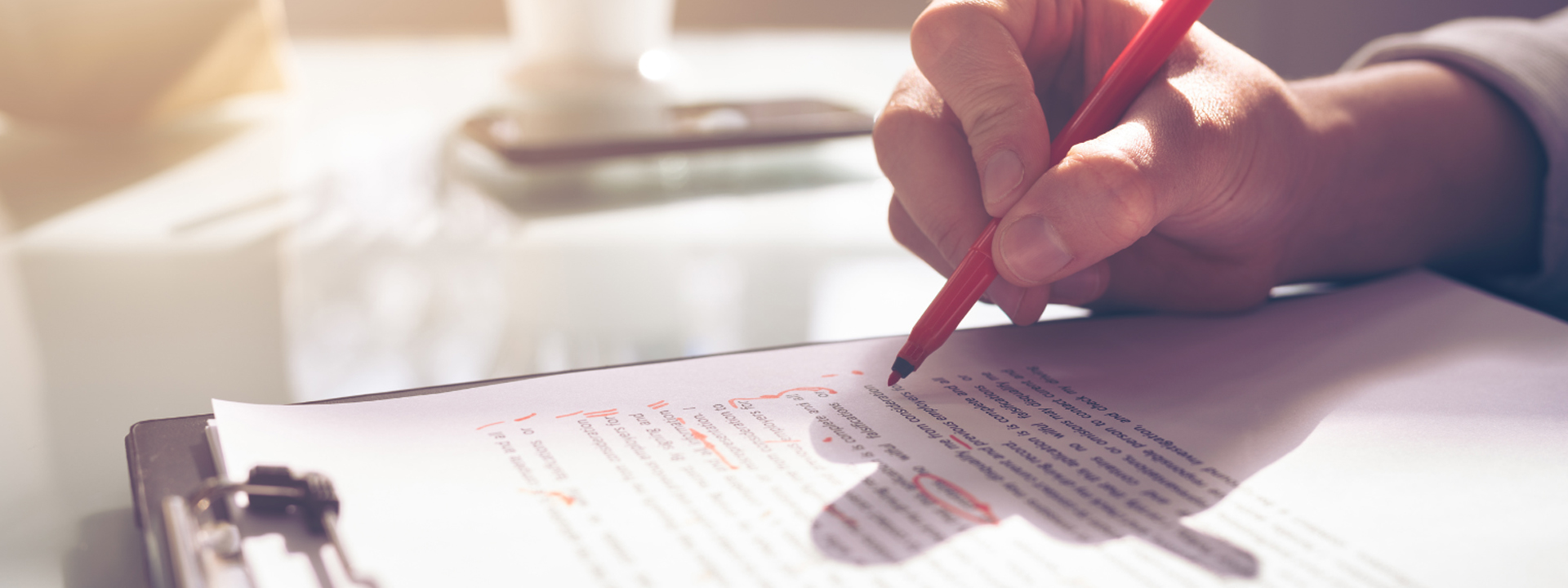 A hand holding a red pen makes corrections on a paper. Image courtesy of Canva