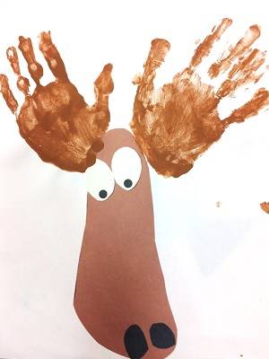 Brown construction paper in the shape of a moose face, with handprints in brown paint representing antlers.