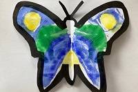 Paper cut in the shape of a butterfly, with symmetrical blue, yellow, and green patterns on both wings.