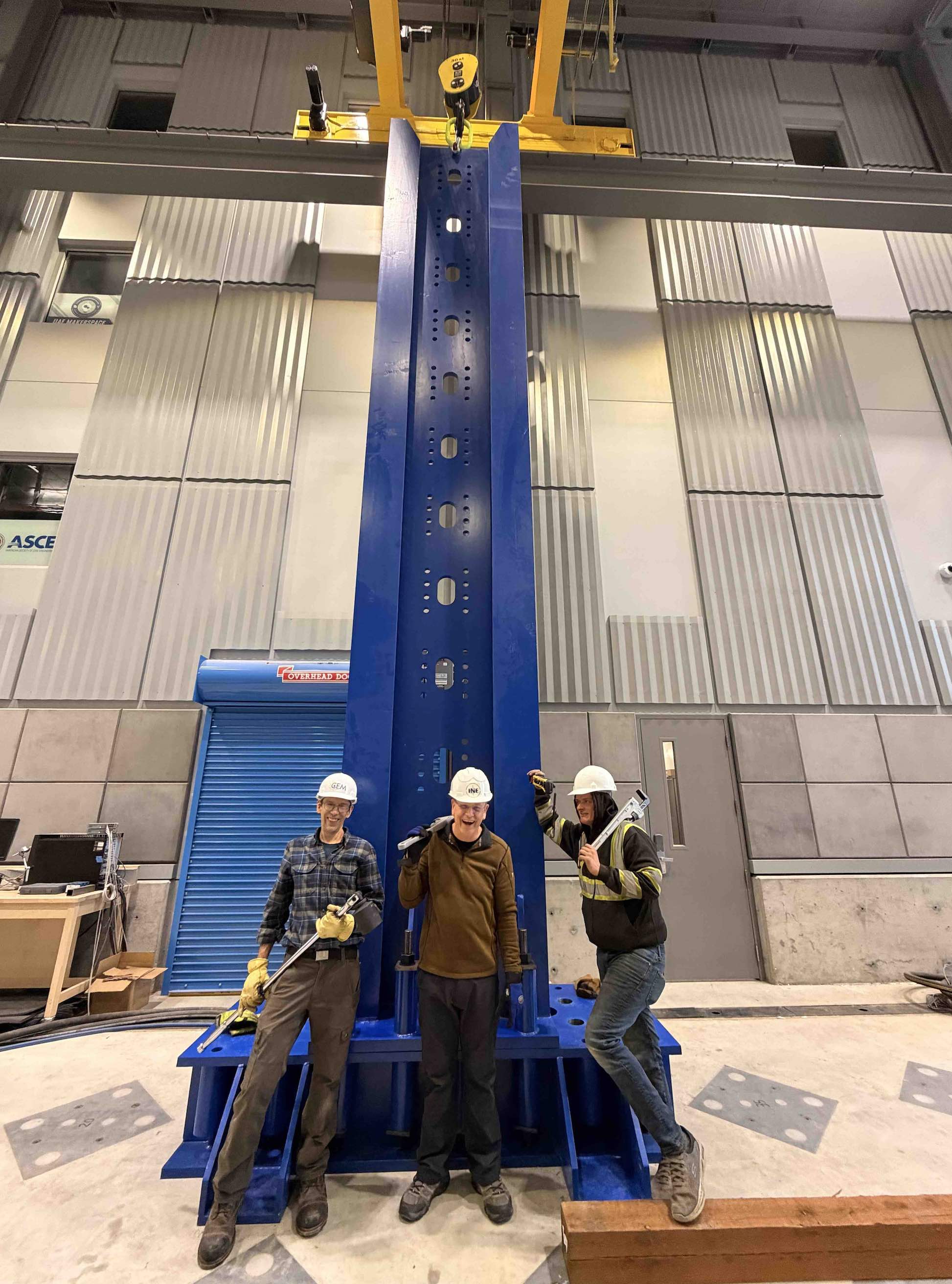 Three people in hard hats pose beside a large multi-story metal structure.