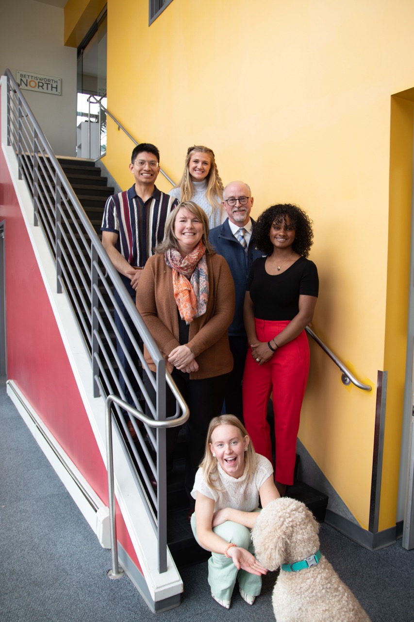 Tracy Vanairsdale (center) stands with CBSM Dean Cameron Carlson, three students, and her dog Copper.