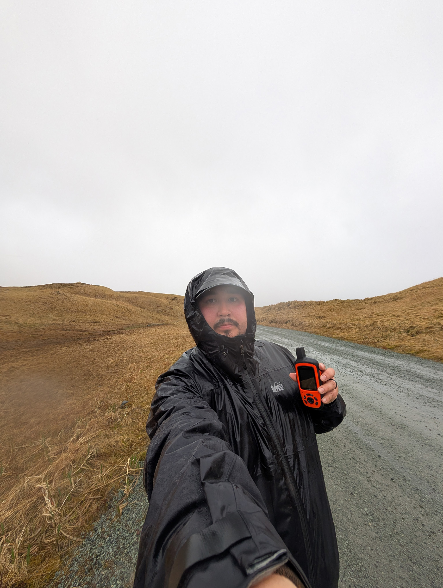 A person in a raincoat holding a GPS device taking a selfie