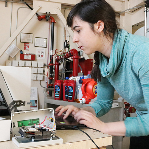 A person testing a fuel consumption monitoring device using an instrument and a laptop.