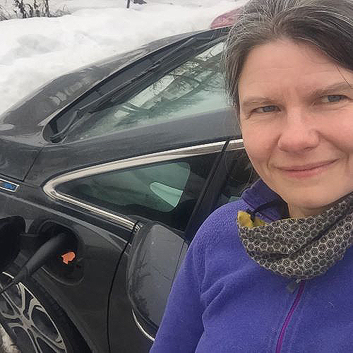 ACEP researcher Michelle Wilber stands with a charging EV