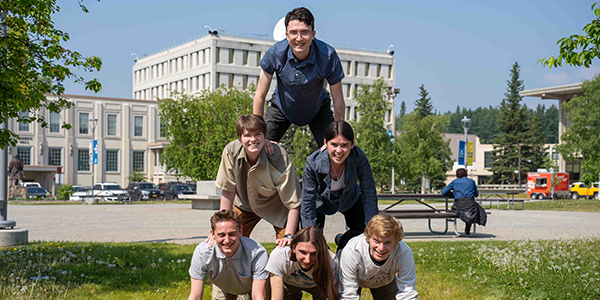 ACEP 2025 summer interns form a human pyramid outside the Usibelli Learning and Innovation Building on the UAF Troth Yeddha’ campus. Pictured (L-R): Glen Ankney, Elliott Lewandowski, Matteo Kuizenga (bottom row), Mackenzie Martin, Emily Cook (middle row), Liam England. Photo by Yuri Bult-Ito/ACEP.