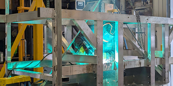 A person is welding the support structure of a hydrokinetic turbine.