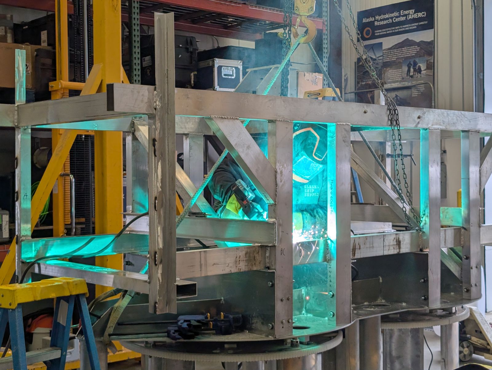 A person is welding the support structure of a hydrokinetic turbine.