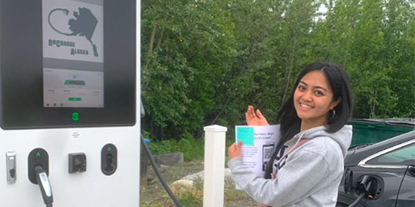 A person holding a sheet of paper stands next to an electric vehicle pump station.
