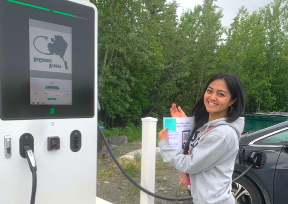 A person holding a sheet of paper stands next to an electric vehicle pump station.