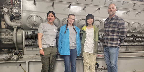 Four people standing in front of a diesel engine.
