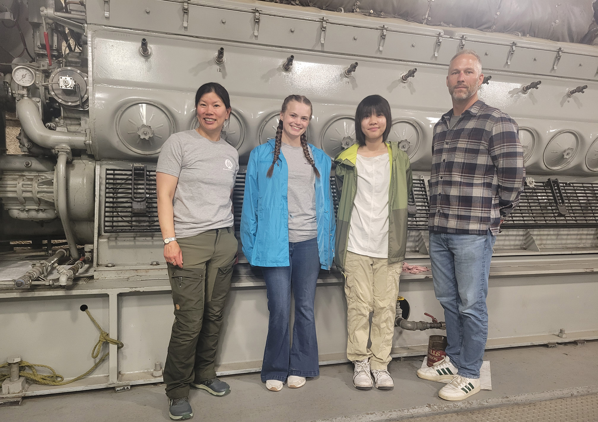 Four people standing in front of a diesel engine.