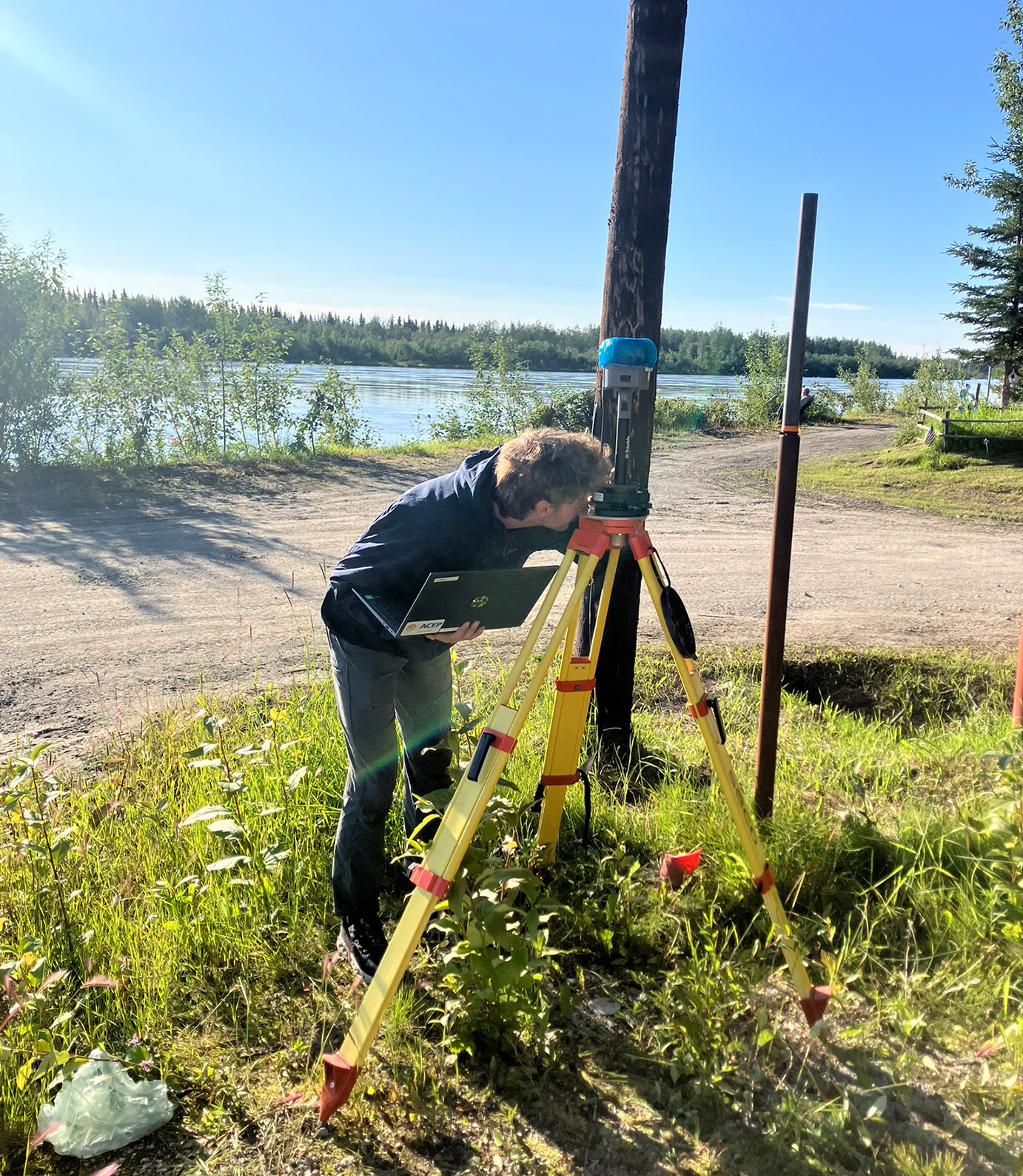 A person is looking at survey equipment by a river
