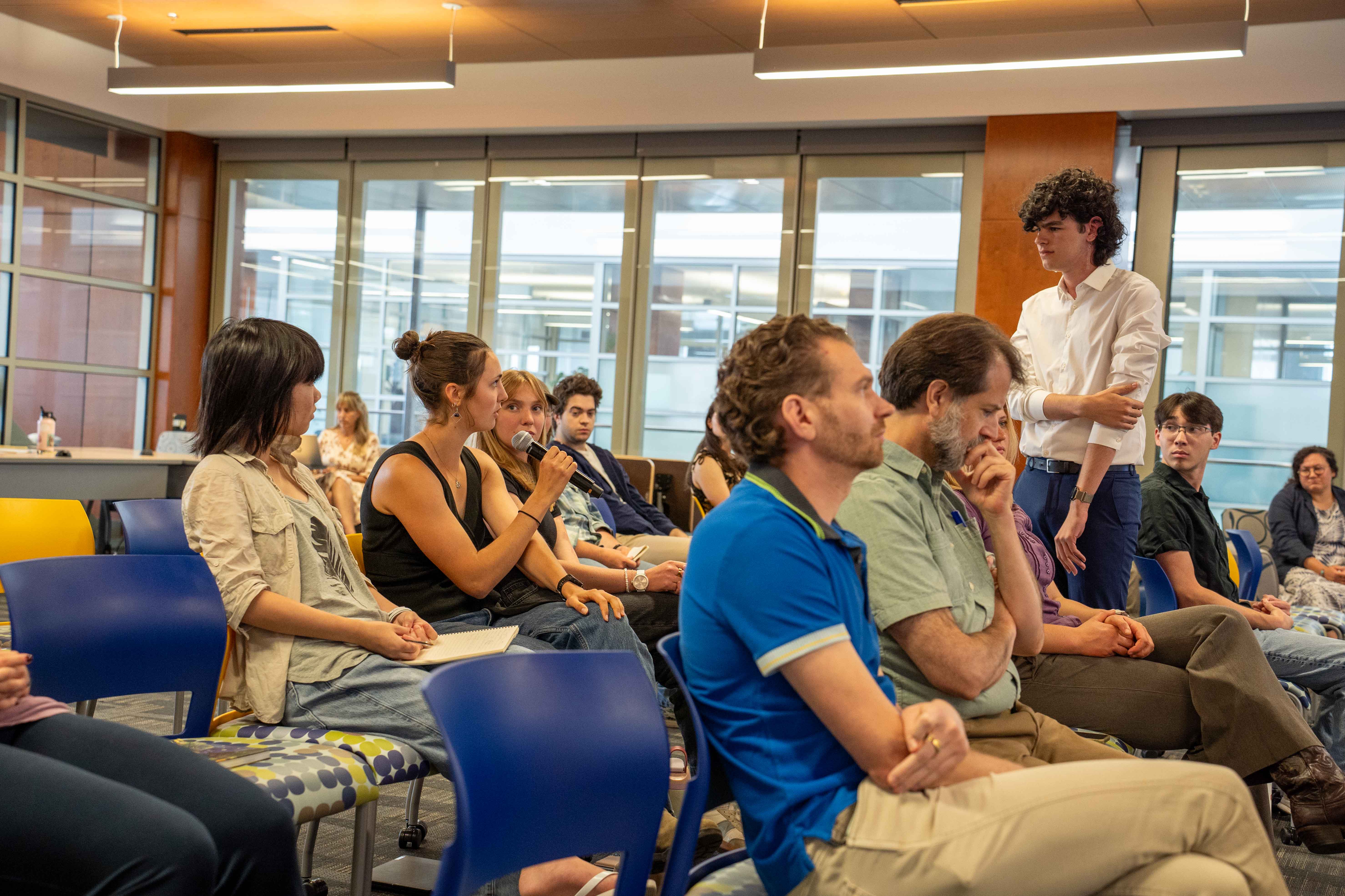 A person in the audience holding a mike talking while a person standing is listening.