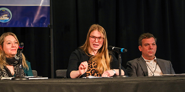 A person is giving a talk with two other panelists sitting on either side