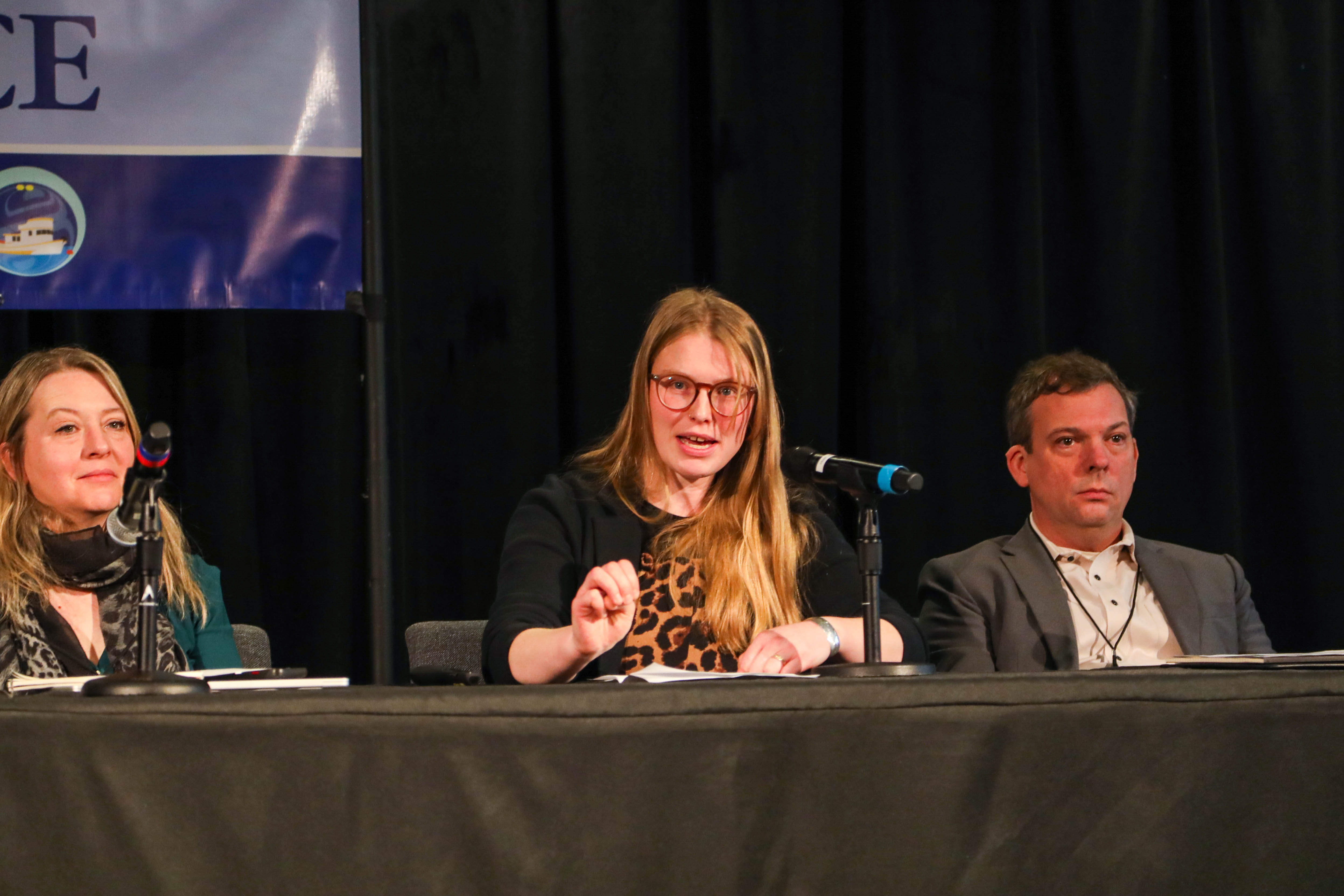 A person is giving a talk on a panel with two people on either side