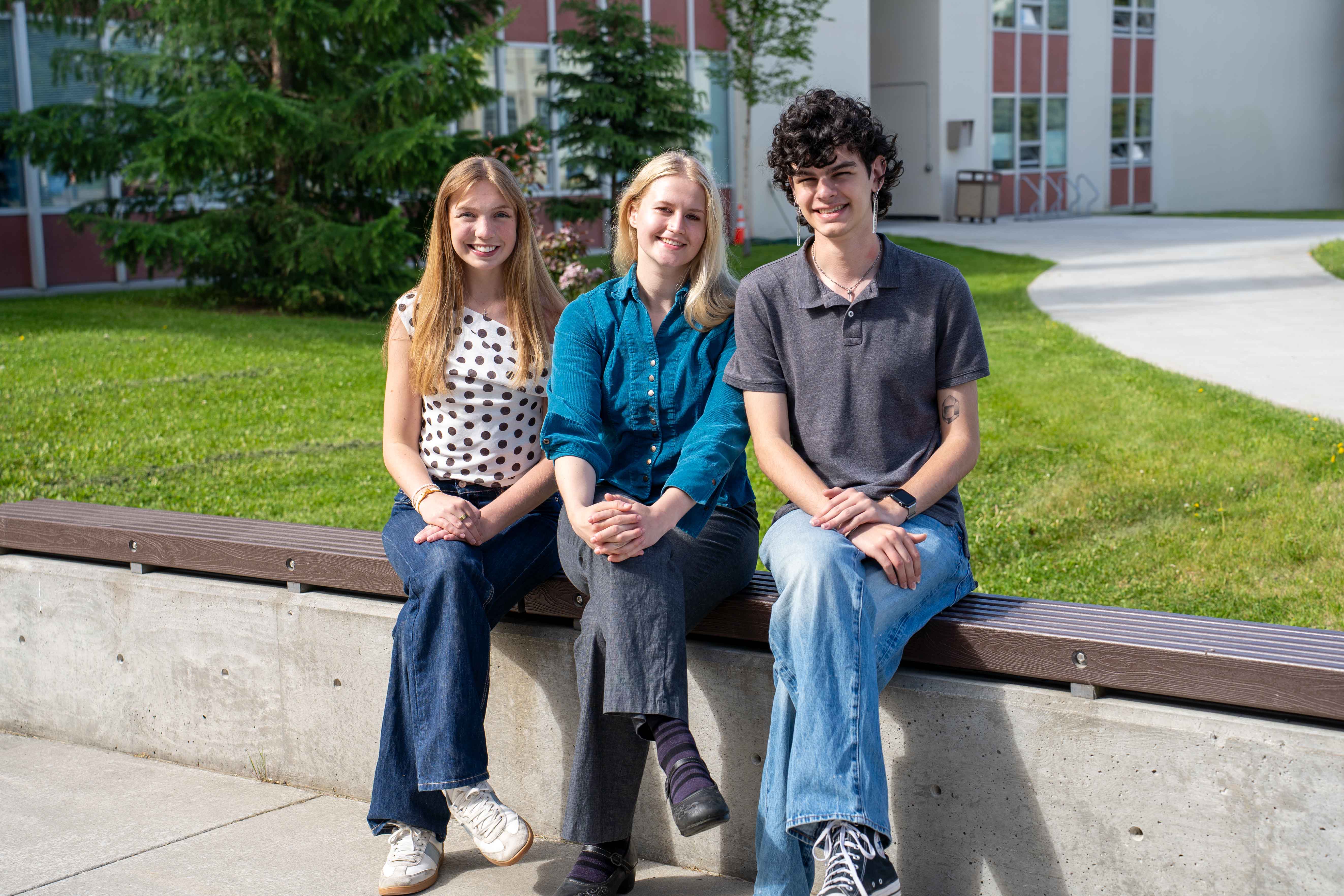 Three people sitting on a bench posing for a photo.