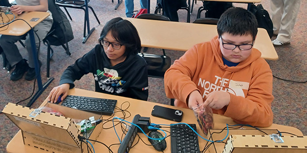 Two teenagers work on computers at a desk