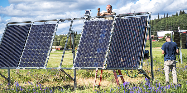 A person working on solar panels, while another person is standing by the panels.