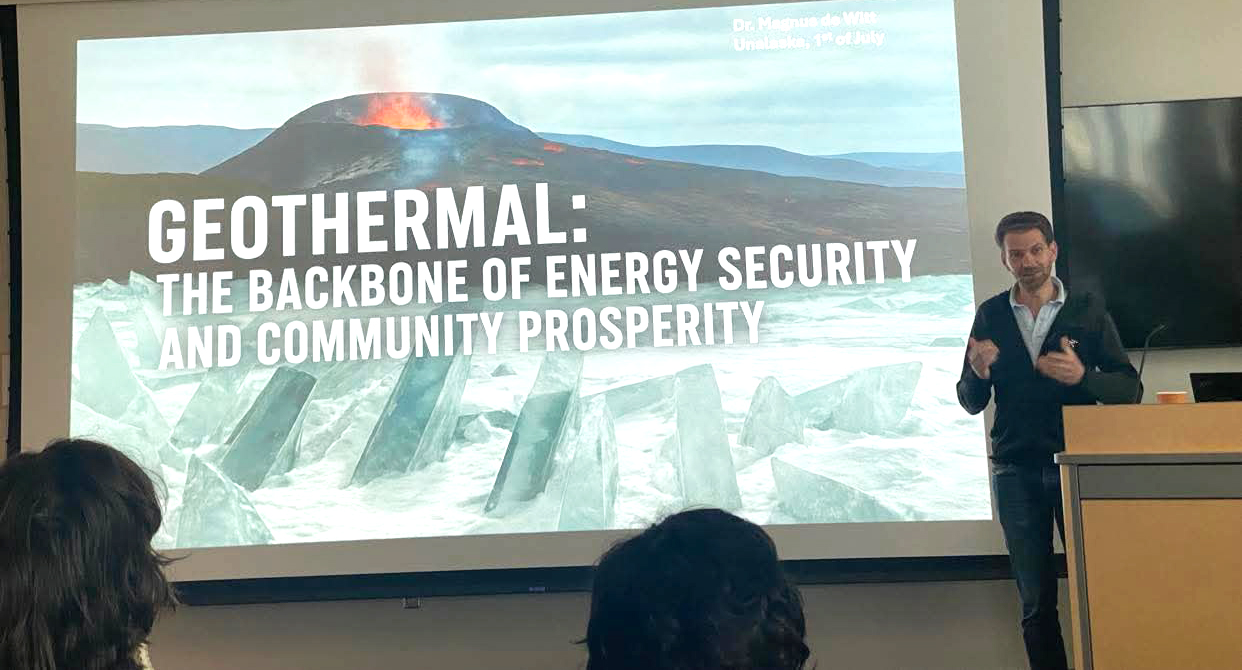 A person is giving a presentation with a slide on geothermal energy behind him.