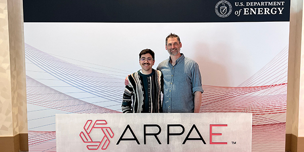 Two people standing side-by-side to pose for a photo with a banner saying ARPA-E in front of them.