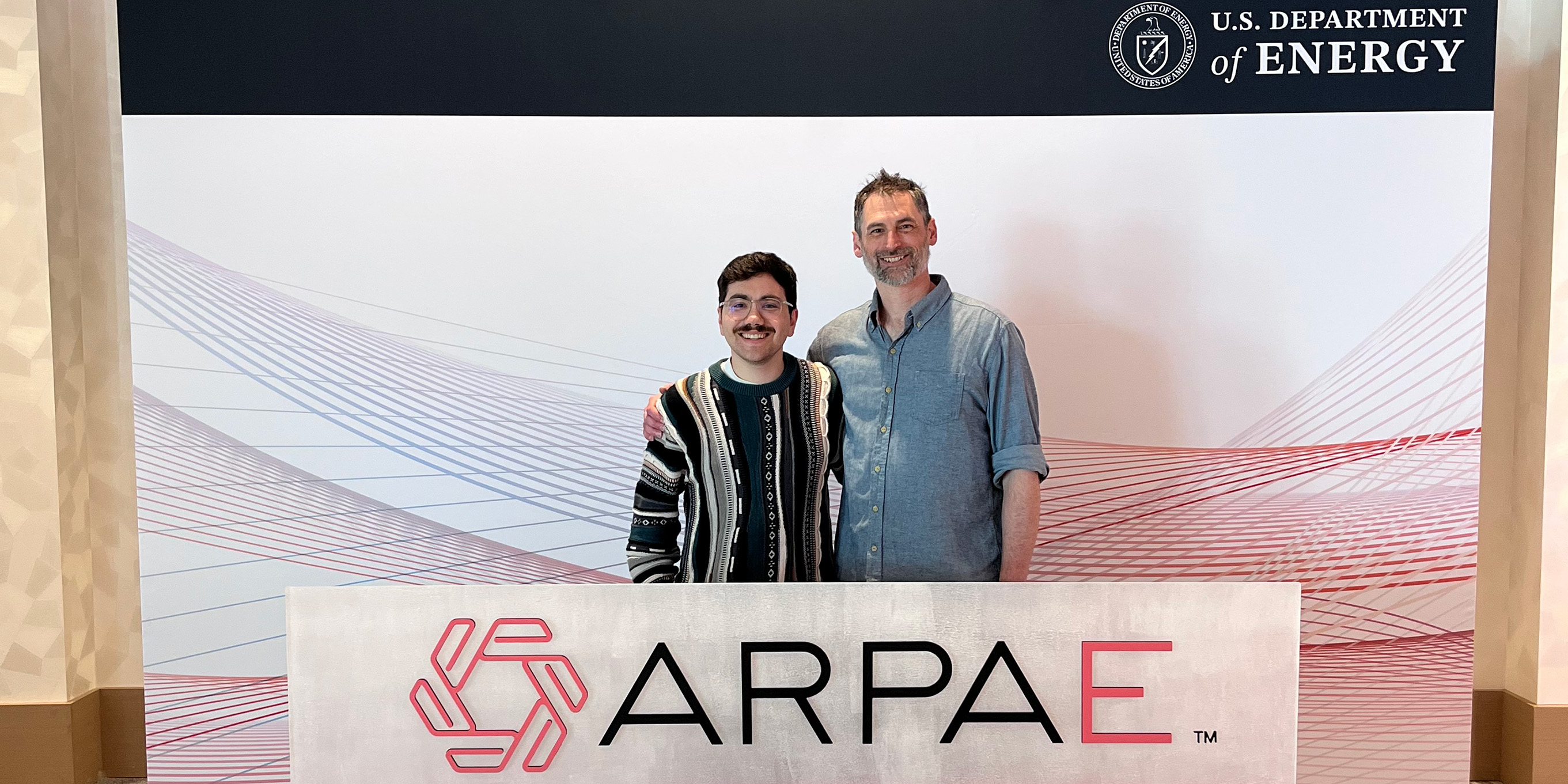 Two people standing side-by-side to pose for a photo with a banner saying ARPA-E in front of them.