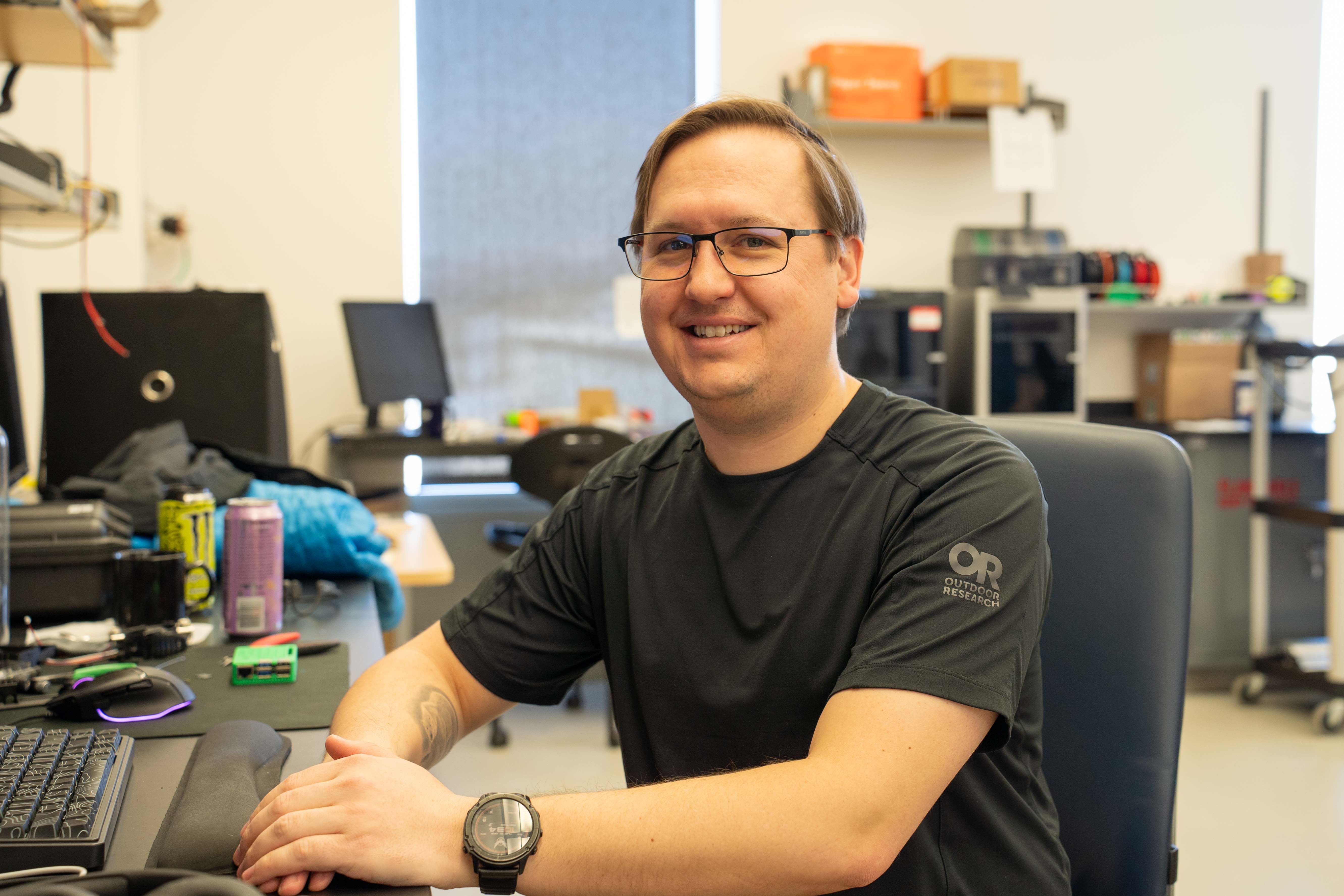 A person sitting at a desk is posing for a photo, smiling
