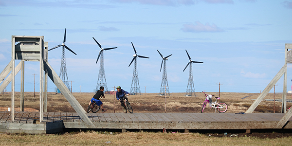 Children ride bikes with wind turbines behind them