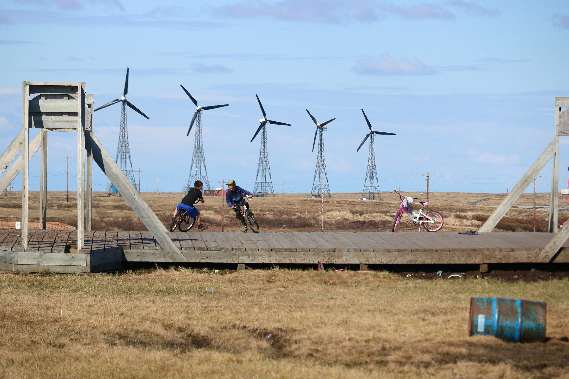 Children ride bikes with wind turbines behind them