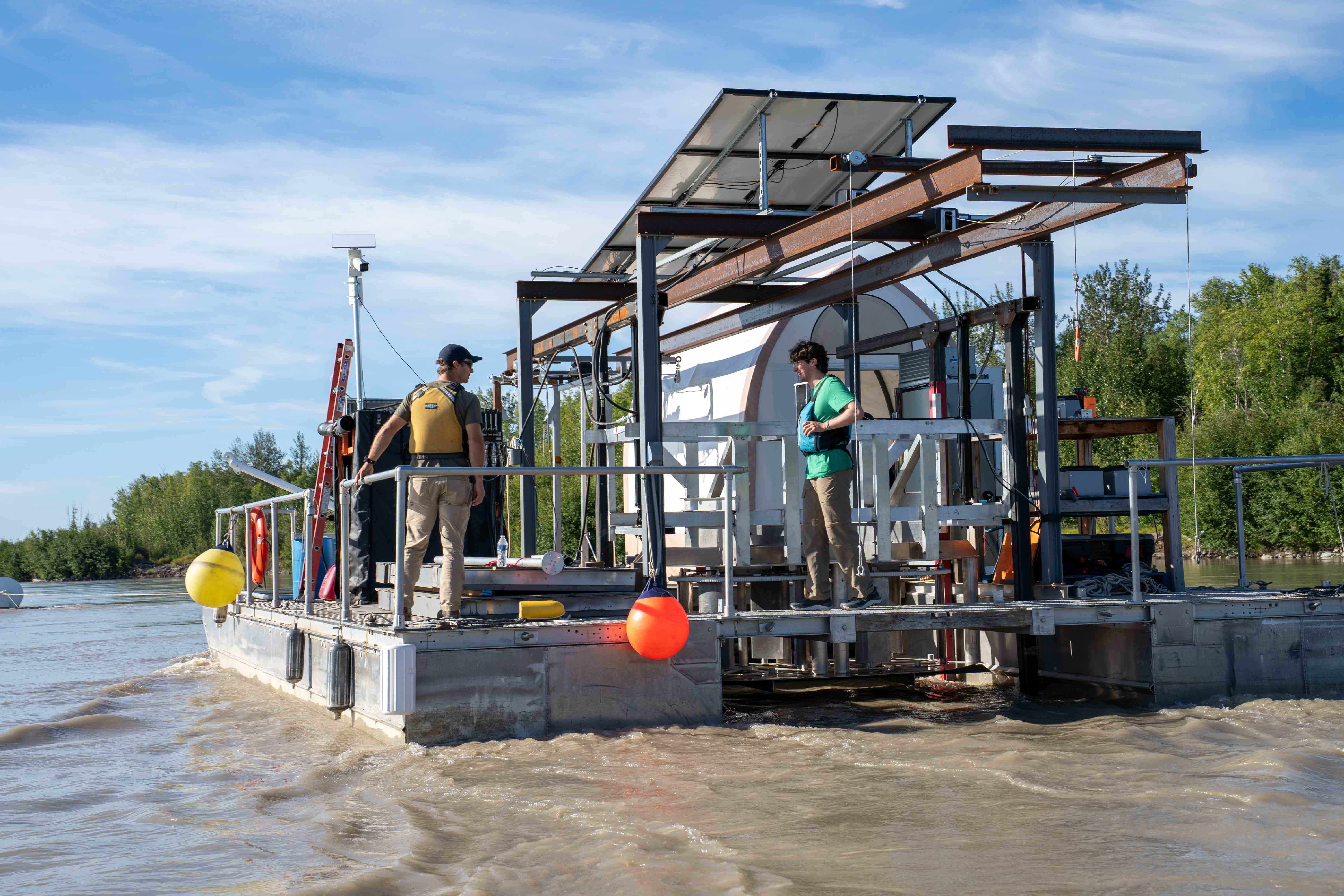 Two people standing on a barge on a river.