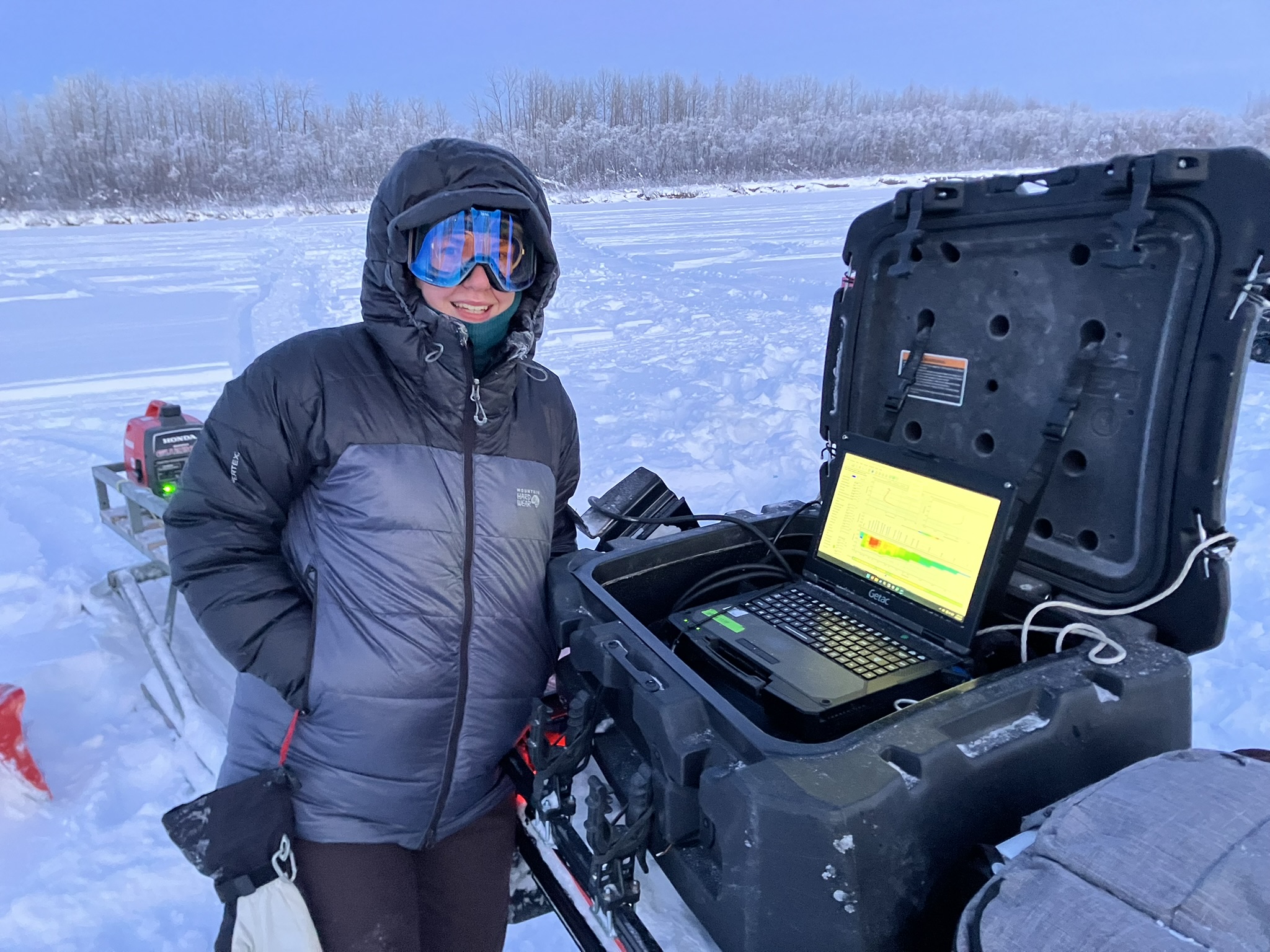 A person stands next to a field laptop on a frozen river
