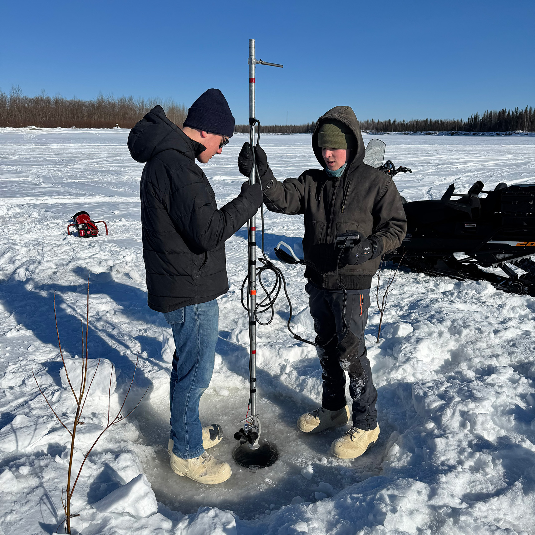 Two people standing with a long measuring tool on a frozen river