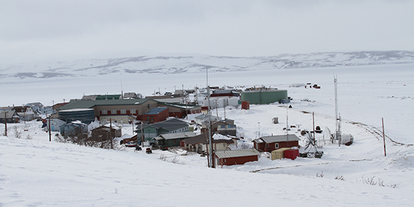 Houses and other buildings in a small Alaska village in winter. Mountains are seen in the far distance.