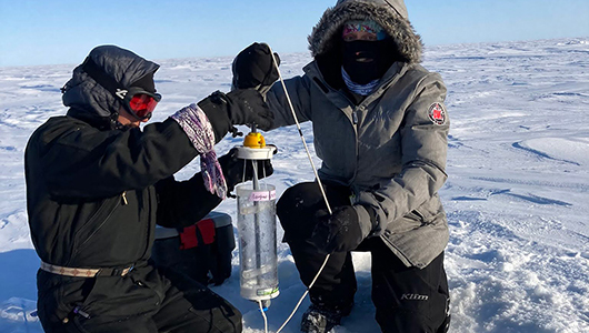 Two researchers working with equipment on the ice.