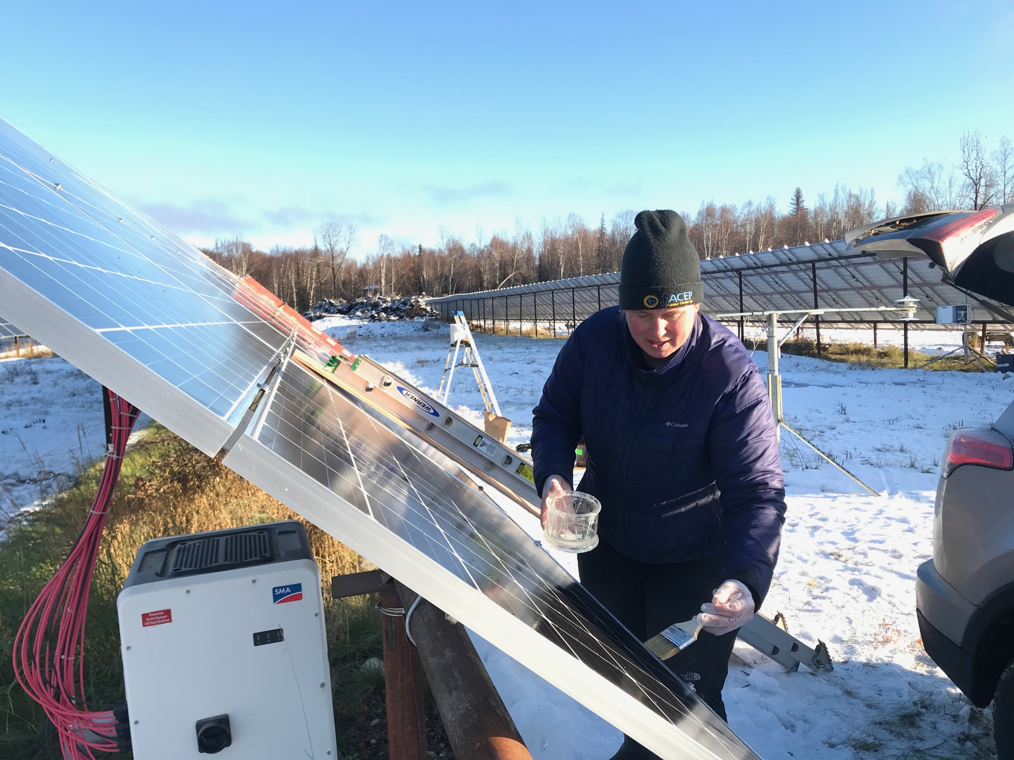 A man brushing a compound on solar panels to assist in snow shedding