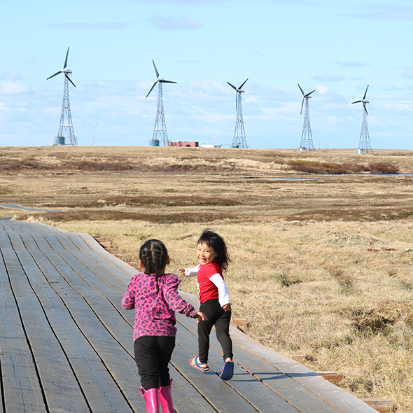 Two children running on boardwalk towards wind powered turbines