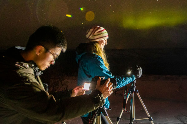 UAF students photograph the aurora on the Fairbanks campus on a winter night.