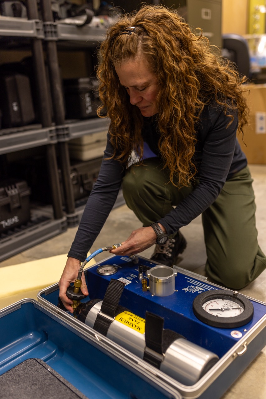 A woman kneels over a high-tech looking briefcase with a pressure chamber inside