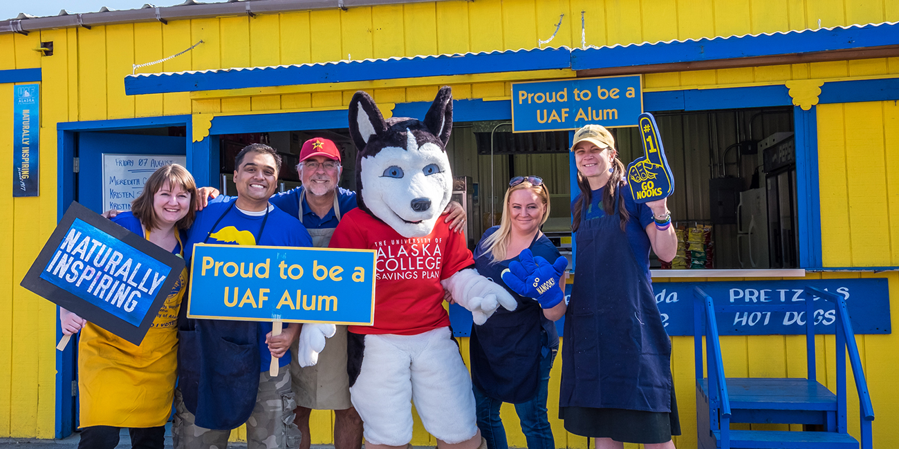 UAF alums Meredith Cameron, Mike Campbell, Todd Paris, Kristin Waggoner and Kristin Sullivan enjoy a visit from Dash the husky during their shift at the Alumni Burger Booth at the 2015 Tanana Valley State Fair.