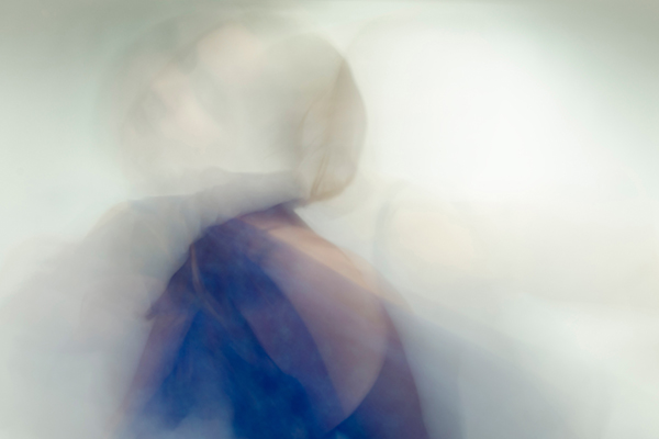 an ethereal long exposure portrait with layers of opacity of a figure in blue looking over her shoulder on a white background