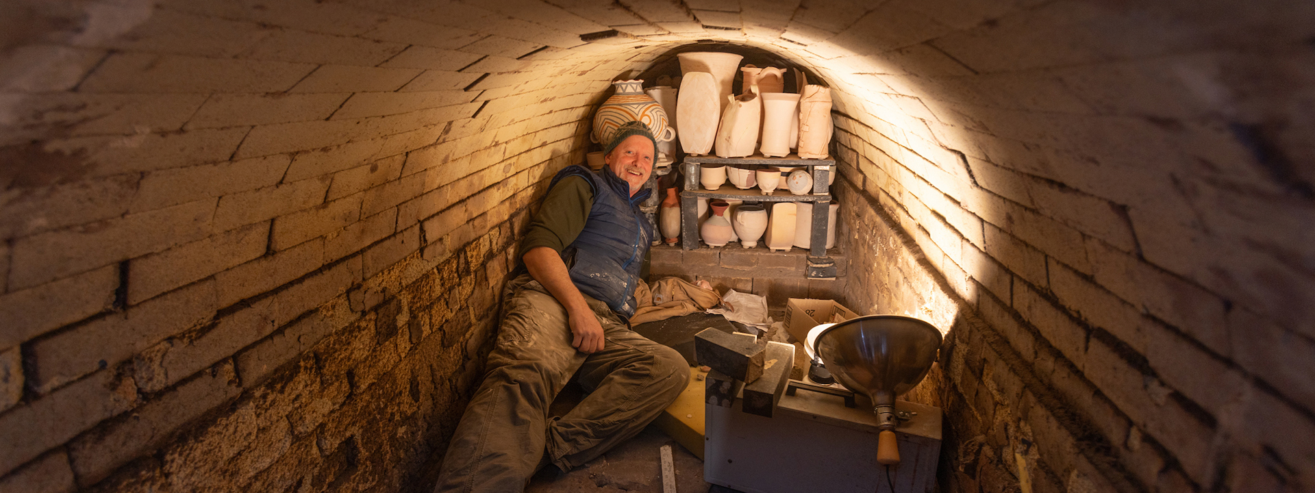 UAF Ceramics Professor and Department Chair Jim Brashear stretches out inside the wood-fired kiln while loading about 400 pottery pieces as he leads students and volunteers in the loading, firing and unloading of the Anagama, or Japanese tunnel kiln, located on the Agricultural and Forestry Experiment Station in April 2024. UAF Photo by Eric Engman
