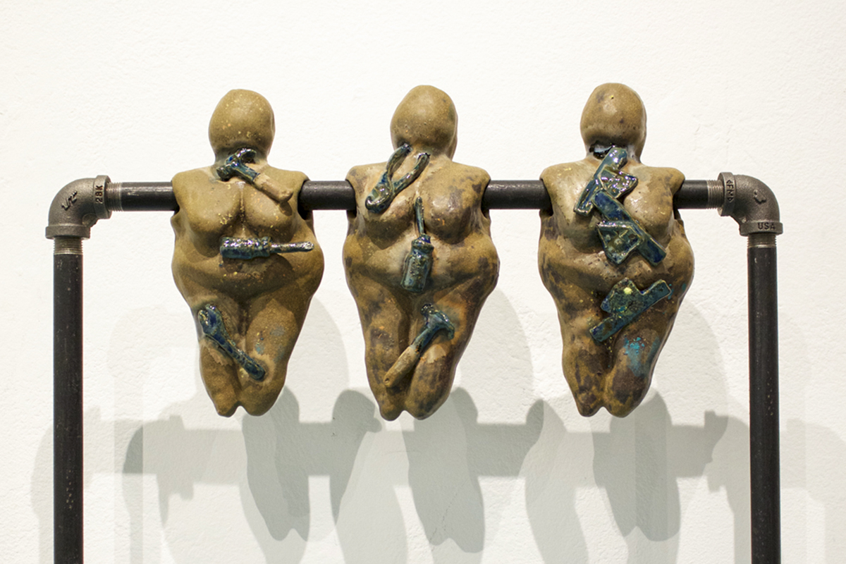 Metal pole through three ceramic goddess figures, each adorned with a ceramic replica of a hand tool