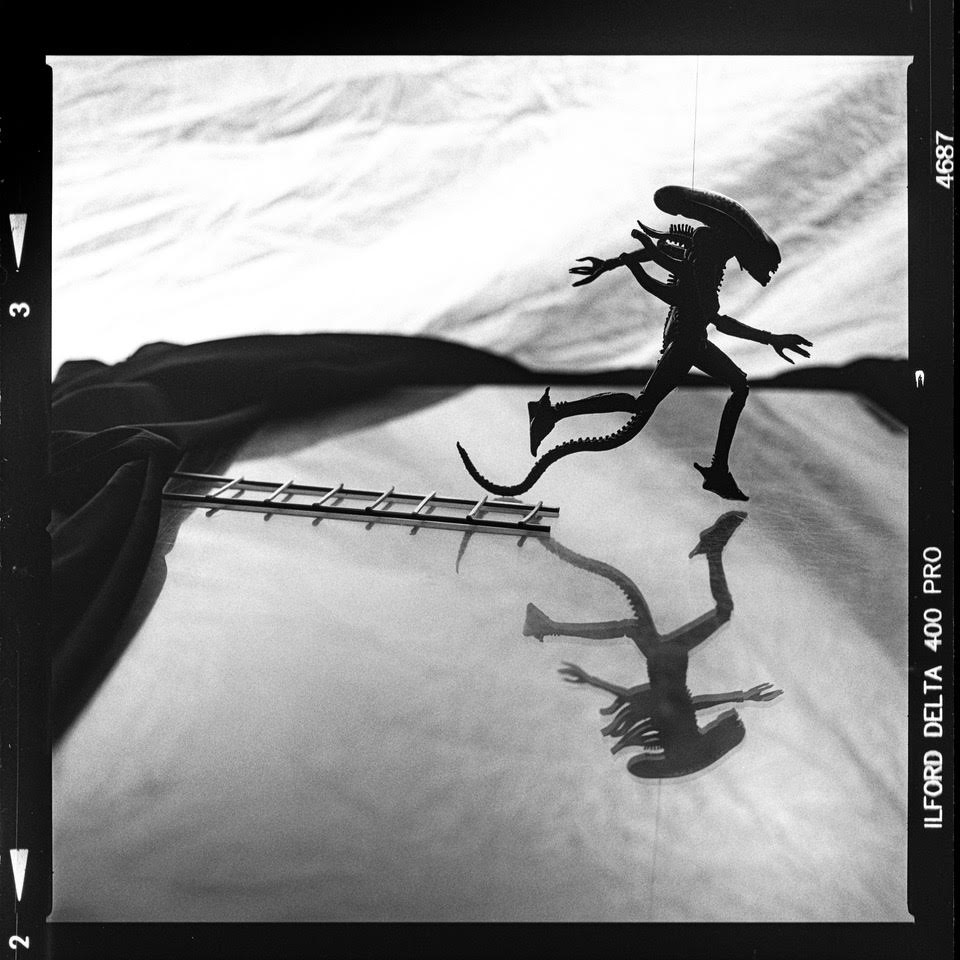 A black and white photo of a toy xenomorph running through the frame