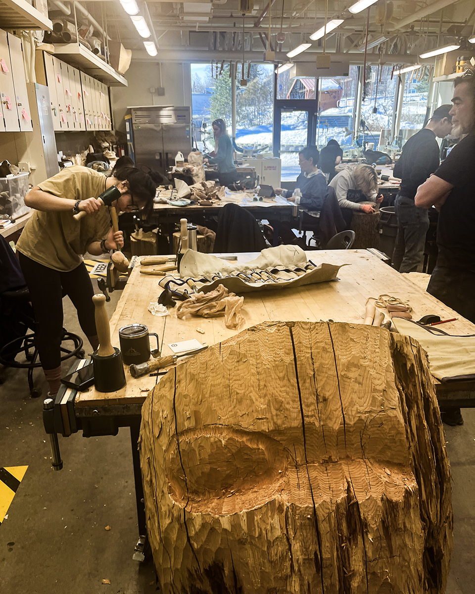 A student in the Native Art Studio chisels a wooden sculpture while Da-ka-xeen Mehner provides guidance. Photo courtesy of the UAF Department of Art