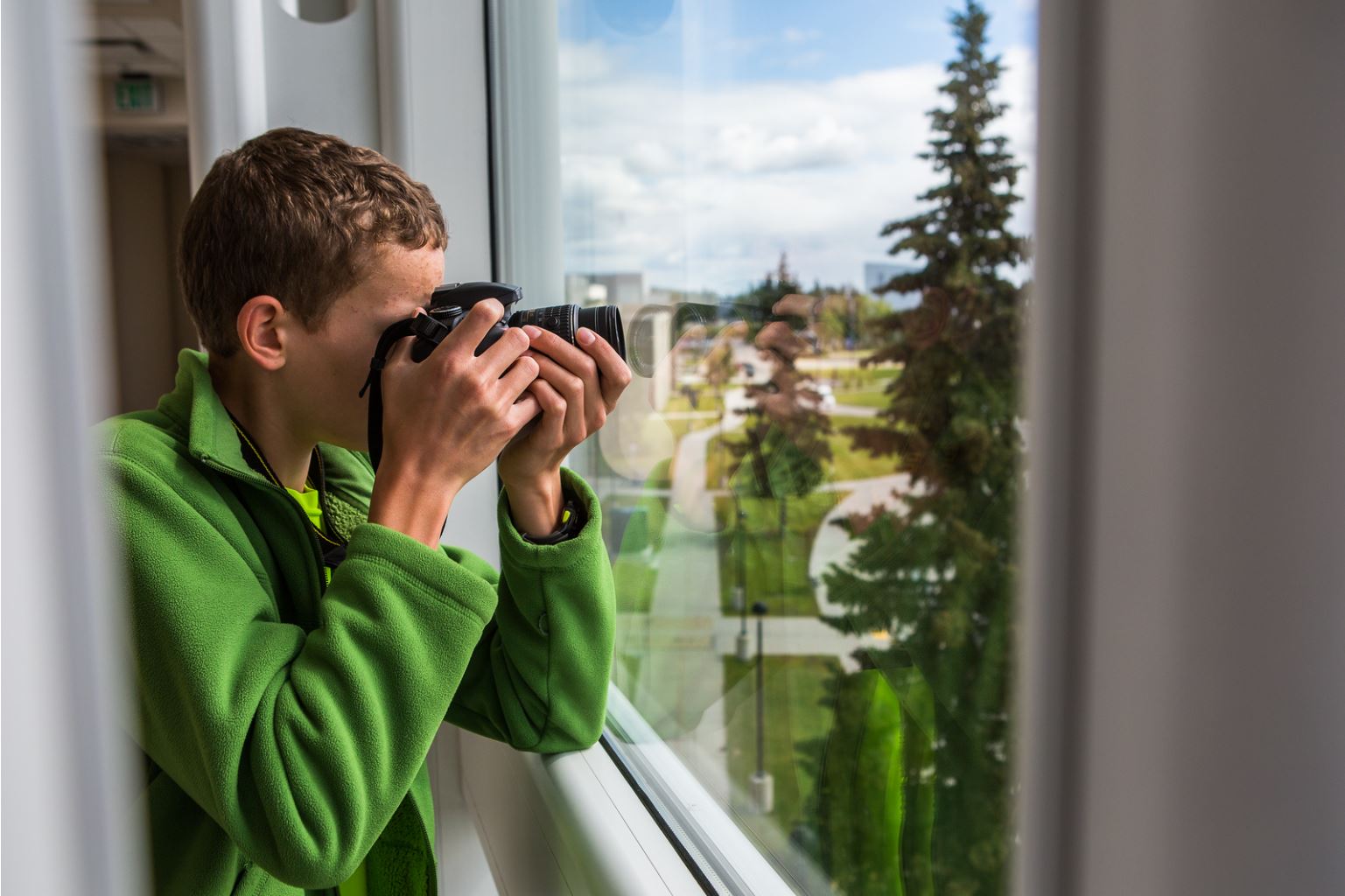 A student takes a photo out a window during the Summer Visual Arts Academy photography class