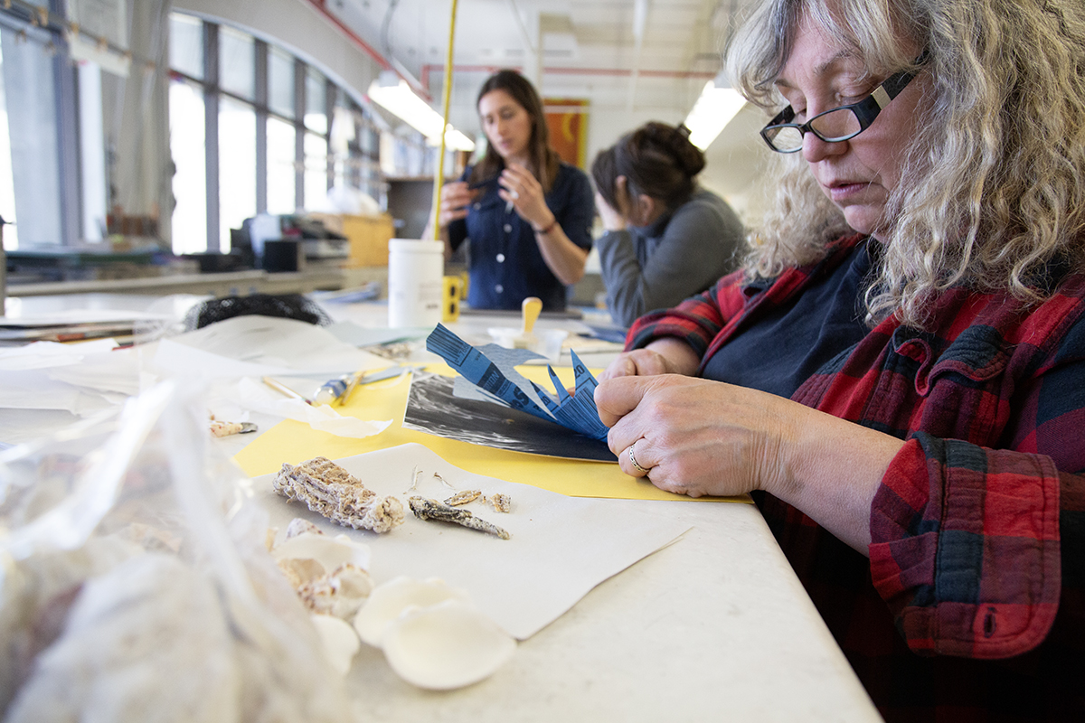 Susan Andrews works on a collagraph print while Sasha Bitzer guides LJ Evans through a printmaking process