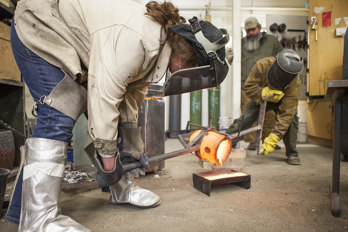 Wendy Croskrey and a student pour molten bronze into a mold in the sculpture studio